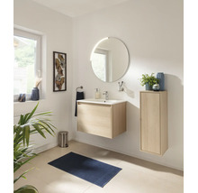 Salle de bains moderne et lumineuse avec meuble sous-vasque suspendu aspect bois, miroir rond, armoire latérale et tapis de bain bleu foncé.