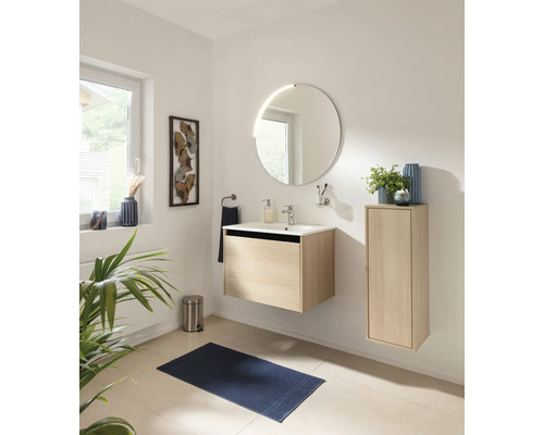 Salle de bain lumineuse avec meuble sous-lavabo suspendu et meuble latéral aspect chêne, lavabo blanc et miroir rond.
