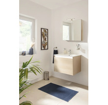 Salle de bains moderne avec meuble sous-lavabo suspendu en bois clair, lavabo blanc, armoire de toilette et tapis de bain bleu.