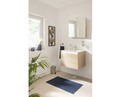 Salle de bains moderne avec meuble sous-lavabo suspendu en bois clair, lavabo blanc, armoire de toilette et tapis de bain bleu.