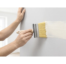 Une personne peint un mur avec un large pinceau et de la peinture blanche.