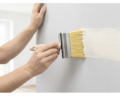 Une personne peint un mur avec un large pinceau et de la peinture blanche.