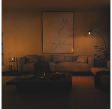 Salon moderne avec un grand tableau mural, un canapé en tissu et un lampadaire à arc avec abat-jour en verre dans une ambiance chaleureuse.