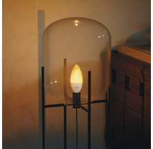 Ampoule LED Philips Hue type flamme éclairant dans une lampe moderne avec abat-jour en verre et cadre en métal noir.