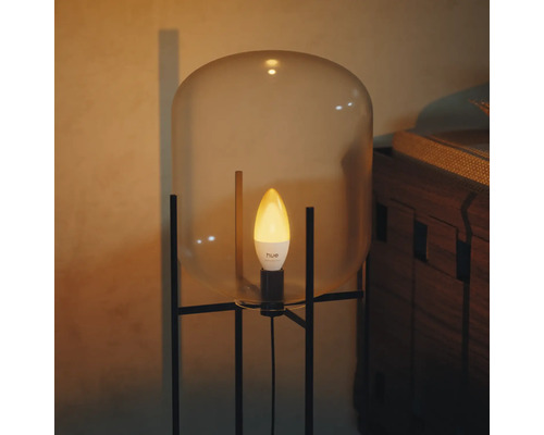 Ampoule LED Philips Hue type flamme éclairant dans une lampe moderne avec abat-jour en verre et cadre en métal noir.