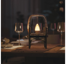 Ampoule LED connectée Philips Hue en forme de flamme éclairée dans une cloche en verre sur une table de salle à manger dressée.