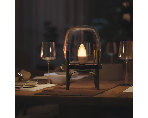 Ampoule LED connectée Philips Hue en forme de flamme éclairée dans une cloche en verre sur une table de salle à manger dressée.