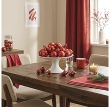 Festlich gedeckter Holztisch mit einer weissen Etagere voller roter Christbaumkugeln, einer Kerze und Adventsdekoration.