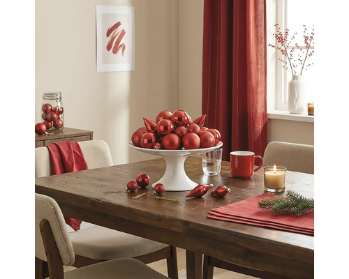 Festlich gedeckter Holztisch mit einer weissen Etagere voller roter Christbaumkugeln, einer Kerze und Adventsdekoration.
