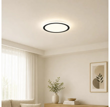 Plafonnier LED rond moderne avec bord noir dans un salon lumineux et minimaliste avec des murs blancs et des meubles clairs.