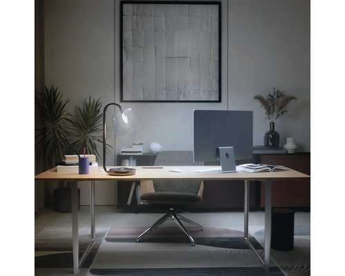 Bureau à domicile moderne avec bureau en bois clair, moniteur, lampe en verre et chaise ergonomique dans une ambiance ordonnée.