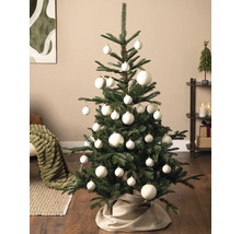 Grüner Weihnachtsbaum geschmückt mit weißen Christbaumkugeln in verschiedenen Größen und einer Baumdecke aus Stoff in einem modernen Wohnzimmer.
