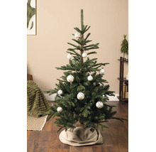 Hell dekorierter künstlicher Weihnachtsbaum in einem Wohnzimmer, geschmückt mit weissen Christbaumkugeln mit Karomuster und einer beigen Baumdecke.
