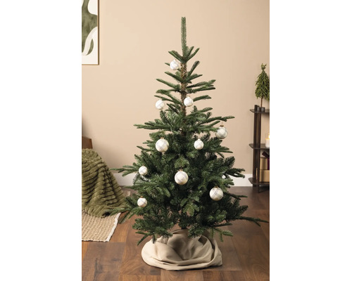 Hell dekorierter künstlicher Weihnachtsbaum in einem Wohnzimmer, geschmückt mit weissen Christbaumkugeln mit Karomuster und einer beigen Baumdecke.