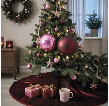 Festlich dekorierter Weihnachtsbaum mit grossen und kleinen Kugeln, Sternen und Lichterkette auf einer dunkelroten Samt-Baumdecke mit Geschenken.