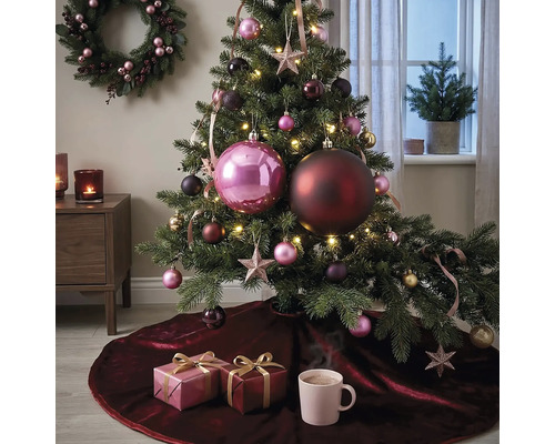 Festlich dekorierter Weihnachtsbaum mit grossen und kleinen Kugeln, Sternen und Lichterkette auf einer dunkelroten Samt-Baumdecke mit Geschenken.