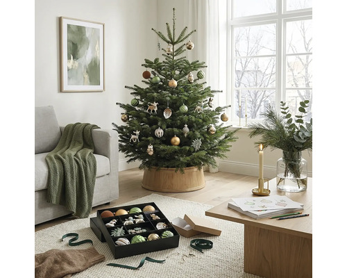 Festlich dekorierter Weihnachtsbaum in einem hellen Wohnzimmer mit Sofa, Holztisch und Weihnachtsschmuck.