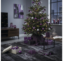 Festlich geschmückter Weihnachtsbaum mit violetten und silbernen Kugeln sowie Sternen in einem modern eingerichteten Wohnzimmer mit Geschenken.