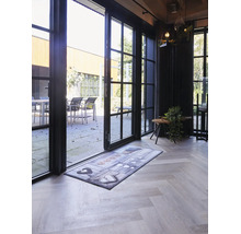 Paillasson avec motif de cœurs devant une porte vitrée ouverte sur un parquet clair en chevrons.