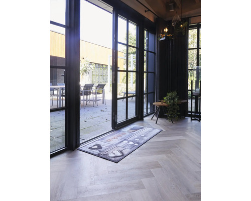 Paillasson avec motif de cœurs devant une porte vitrée ouverte sur un parquet clair en chevrons.