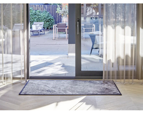 Paillasson rectangulaire aspect marbre devant une baie vitrée sur un parquet clair dans un intérieur moderne.