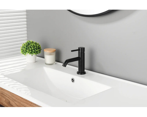 Mitigeur de lavabo noir moderne sur un lavabo blanc dans une salle de bains lumineuse avec une plante et une bougie.