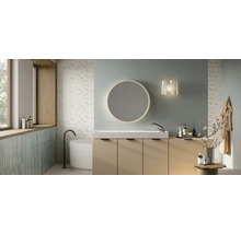 Modernes Badezimmer mit beigem Waschtischunterschrank, weißem Waschbecken, rundem Spiegel und freistehender Badewanne vor floralen Fliesen.
