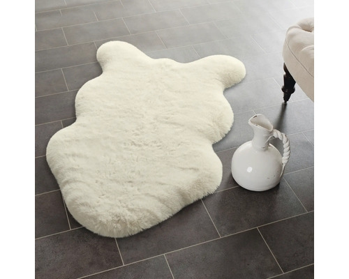 Weiches Kunstfell in Schaffelloptik auf dunklen Bodenfliesen neben einem dekorativen Krug.