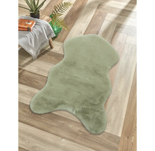 Tapis vert en fourrure synthétique en forme de peau de mouton sur un sol en bois à chevrons à côté d'une table d'appoint avec couverture.