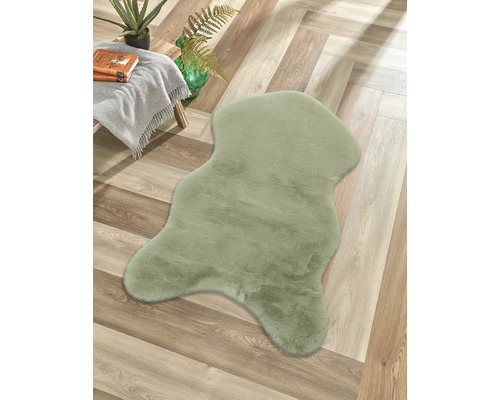 Tapis vert en fourrure synthétique en forme de peau de mouton sur un sol en bois à chevrons à côté d'une table d'appoint avec couverture.