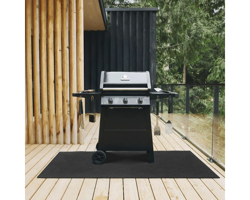 Schwarzer Gasgrill mit drei Reglern und Grillbesteck auf einer schwarzen Bodenschutzmatte auf einer Holzterrasse.