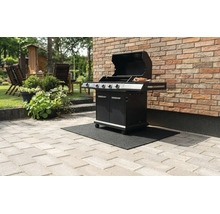 Schwarzer Gasgrill mit offenem Deckel auf einer schwarzen Grillbodenschutzmatte auf einer Steinterrasse vor einer Backsteinwand.