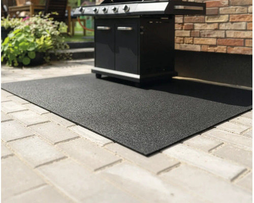 Schwarze, strukturierte Grillschutzmatte auf einer gepflasterten Terrasse unter einem Gasgrill.