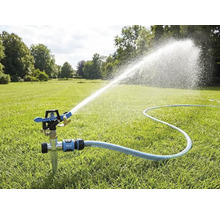 Arroseur par impulsions avec piquet sur une pelouse, raccordé à un tuyau d'arrosage, projetant un jet d'eau pour l'arrosage du jardin.