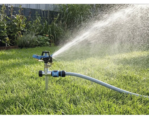 Arroseur à impulsion avec pic sur une pelouse, raccordé à un tuyau d'arrosage, projetant de l'eau en un large jet.