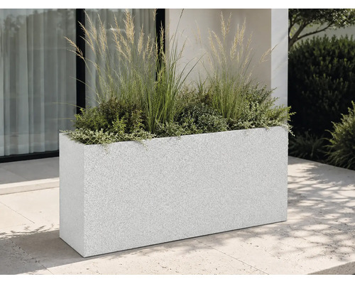 Bac à fleurs rectangulaire aspect granit sur une terrasse moderne, garni de graminées ornementales et de plantes devant une façade.