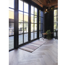 Salon lumineux avec de grandes portes-fenêtres noires, un tapis rayé et un sol avec un motif en chevrons.
