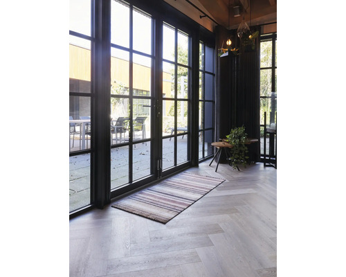 Salon lumineux avec de grandes portes-fenêtres noires, un tapis rayé et un sol avec un motif en chevrons.