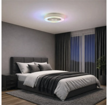 Moderner Deckenventilator mit farbigem LED-Lichtring in einem Schlafzimmer mit grauem Polsterbett, dunklen Vorhängen und Teppich.