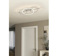 Plafonnier LED moderne avec quatre anneaux entrelacés dans une pièce lumineuse avec une porte blanche et un décor minimaliste.