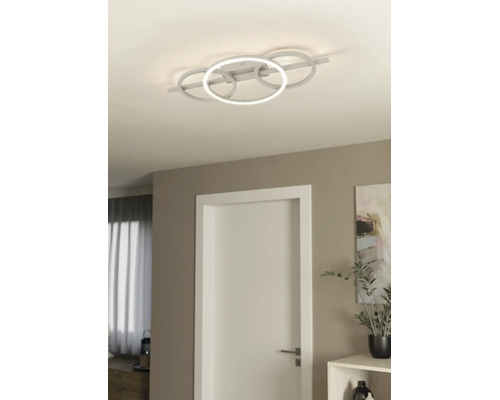 Plafonnier LED moderne avec quatre anneaux entrelacés dans une pièce lumineuse avec une porte blanche et un décor minimaliste.