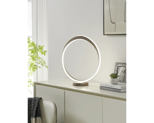 Moderne LED-Tischleuchte in kreisförmigem Ring-Design auf einer Kommode. Hell eingerichteter Raum mit Pflanze, Büchern und Bilderrahmen.