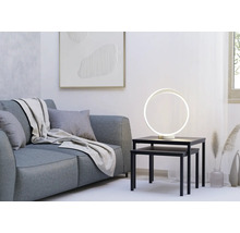 Moderne ringförmige LED-Tischleuchte auf schwarzen Satztischen neben einem grauen Sofa in einem hellen, minimalistischen Wohnzimmer.