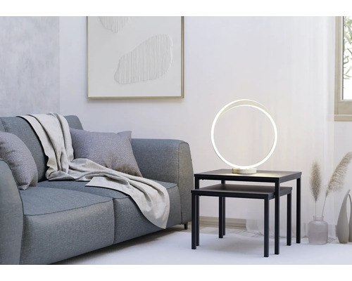 Moderne ringförmige LED-Tischleuchte auf schwarzen Satztischen neben einem grauen Sofa in einem hellen, minimalistischen Wohnzimmer.
