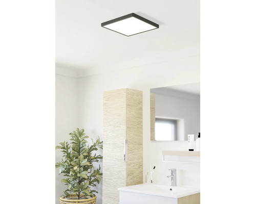Salle de bains lumineuse avec plafonnier LED carré, lavabo moderne, armoire haute aspect bois et plante d intérieur.