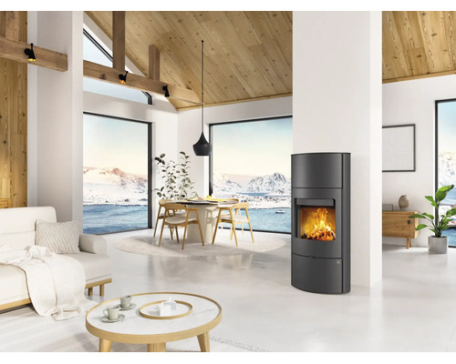 Poêle à bois moderne dans un salon lumineux avec de hauts plafonds, des poutres en bois et des fenêtres panoramiques sur un paysage enneigé.