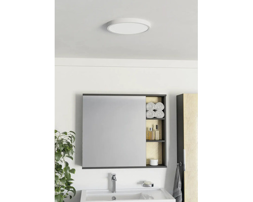 Salle de bain moderne avec armoire de toilette, étagère ouverte, lavabo blanc, robinetterie chromée et plafonnier rond.