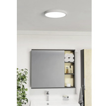 Salle de bains lumineuse avec plafonnier rond, armoire de toilette à étagères ouvertes pour serviettes et produits de soin et lavabo blanc.