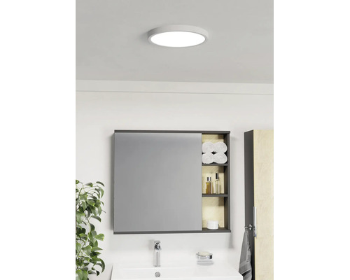 Salle de bains lumineuse avec plafonnier rond, armoire de toilette à étagères ouvertes pour serviettes et produits de soin et lavabo blanc.