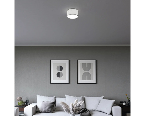 Plafonnier cylindrique moderne dans un salon minimaliste avec canapé et tableaux abstraits sur un mur gris.